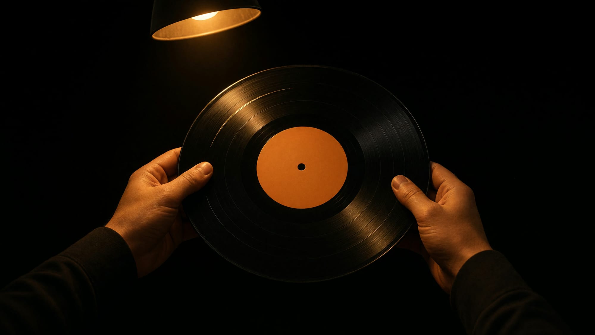 Two hands holding a twelve-inch record by its edges under a desk lamp